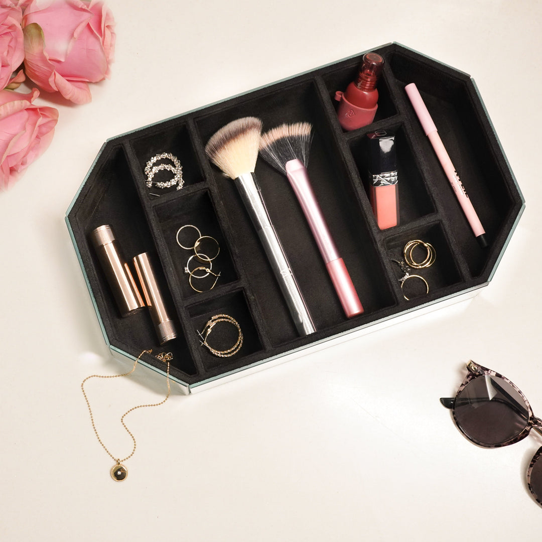 Mirror glass vanity organiser with black suede sections holding makeup brushes, lipsticks and jewellery