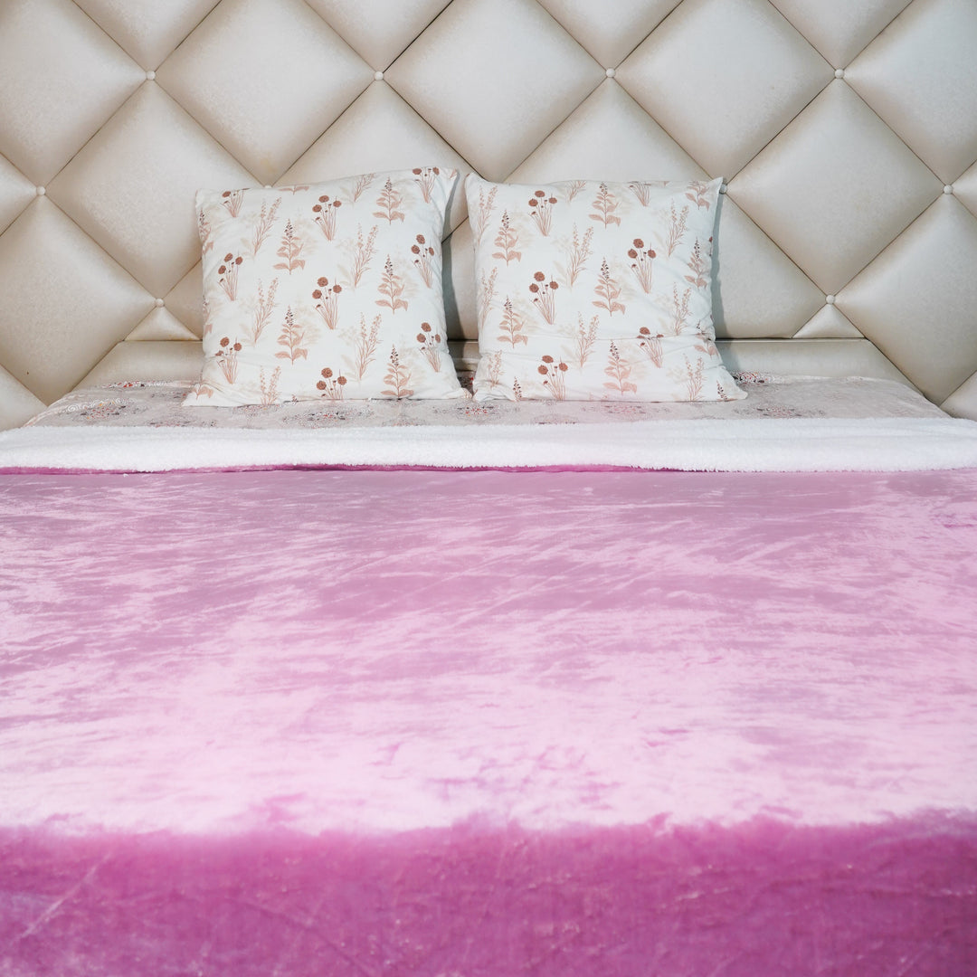 Pink plush sherpa throw blanket spread on a bed with patterned cushions