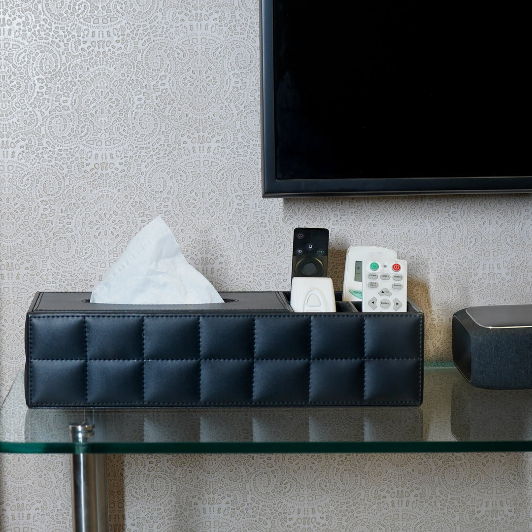 Black faux leather multi-purpose organiser with tissue holder and remotes on a glass coffee table